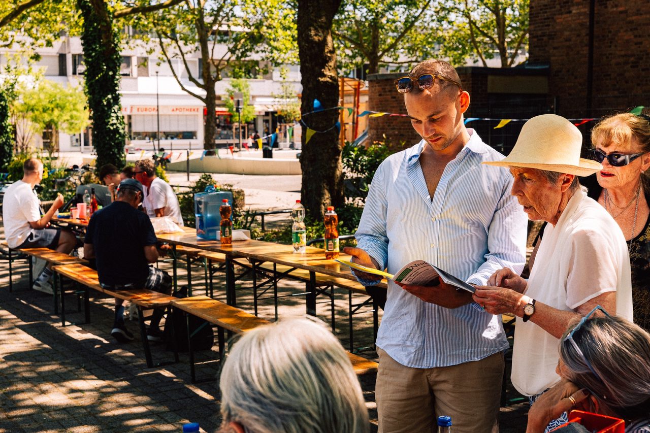Leonard Kordowski zeigt zwei Frauen Informationsmaterial im Biergarten