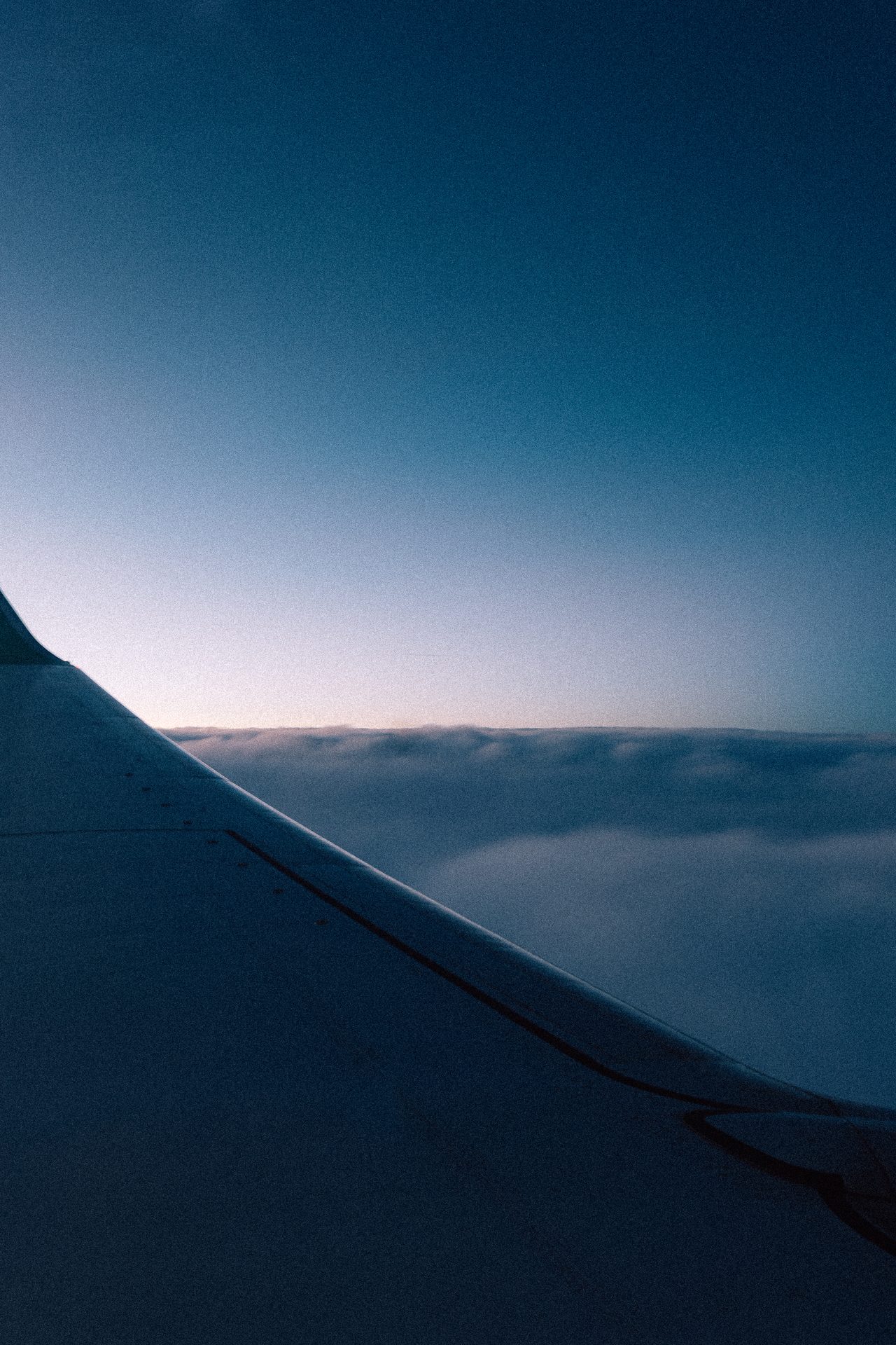 Ein Flugzeugflügel über Wolken unter einem blaurosa Himmel.
