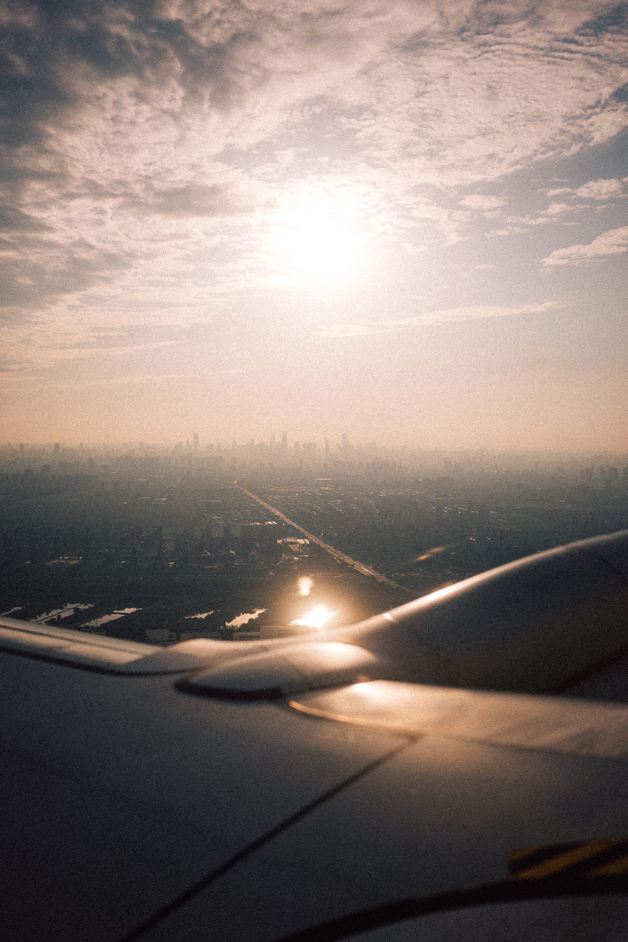 Ein Flugzeugflügel vor tief stehender Sonne über einer dunstigen Stadt.