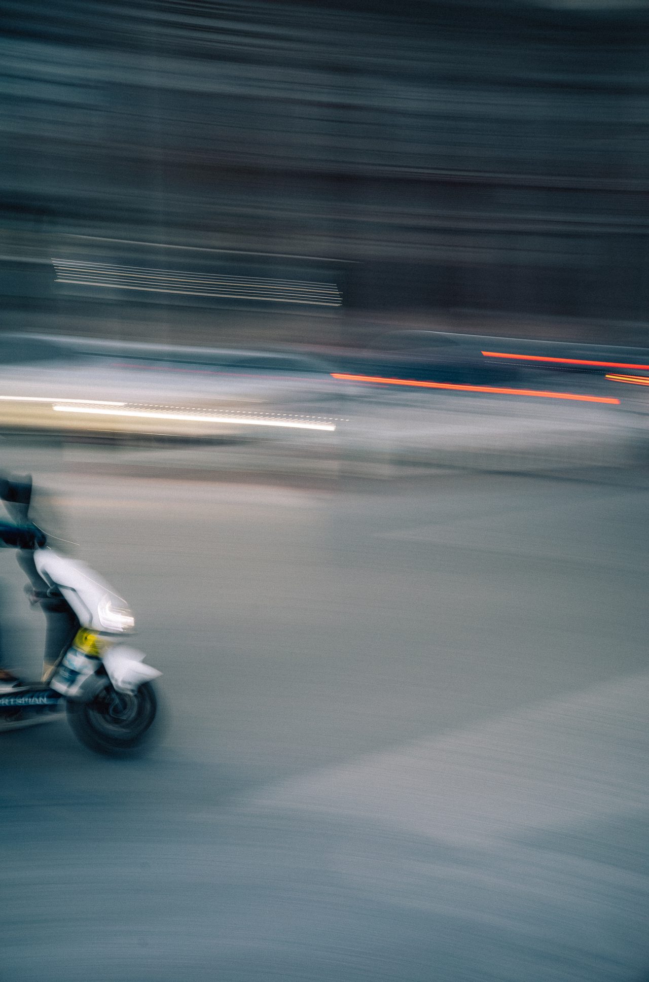 Ein Motorroller zieht verwischt durch eine städtische Straße.