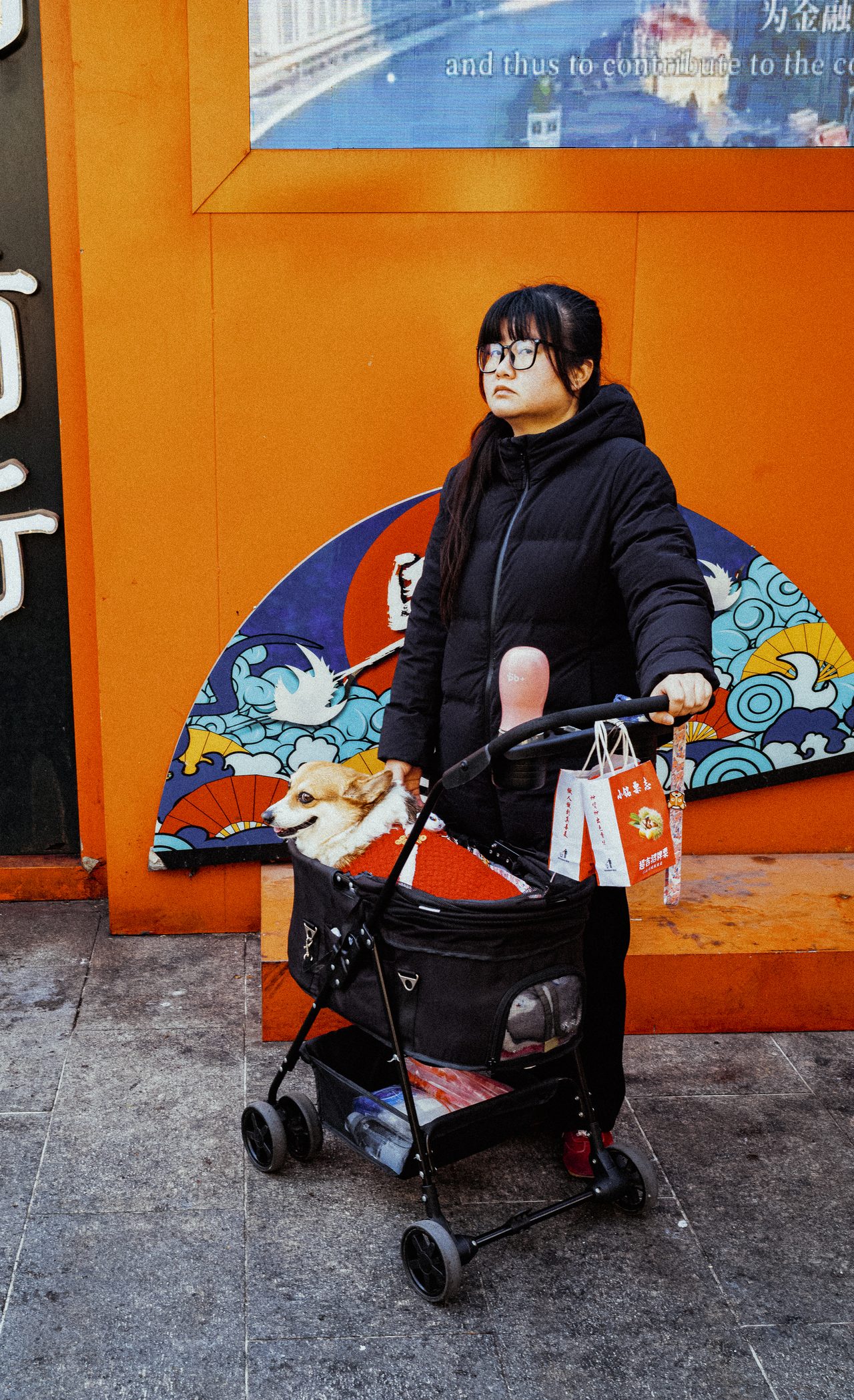 Eine Frau mit Rollator steht vor einer orangefarbenen Wand mit Wandmalerei.