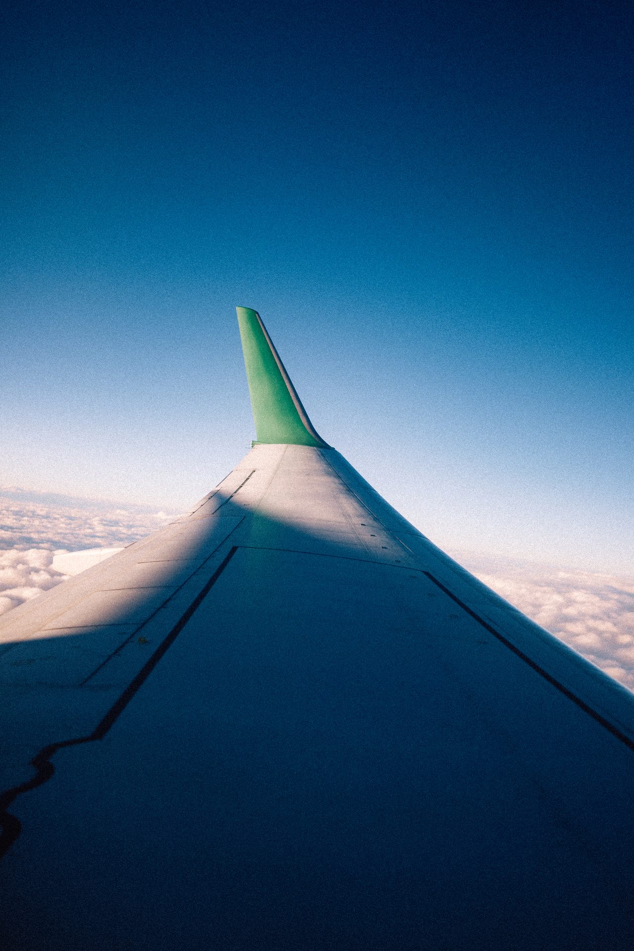 Eine grüne Flügelspitze über Wolken vor tiefblauem Himmel.