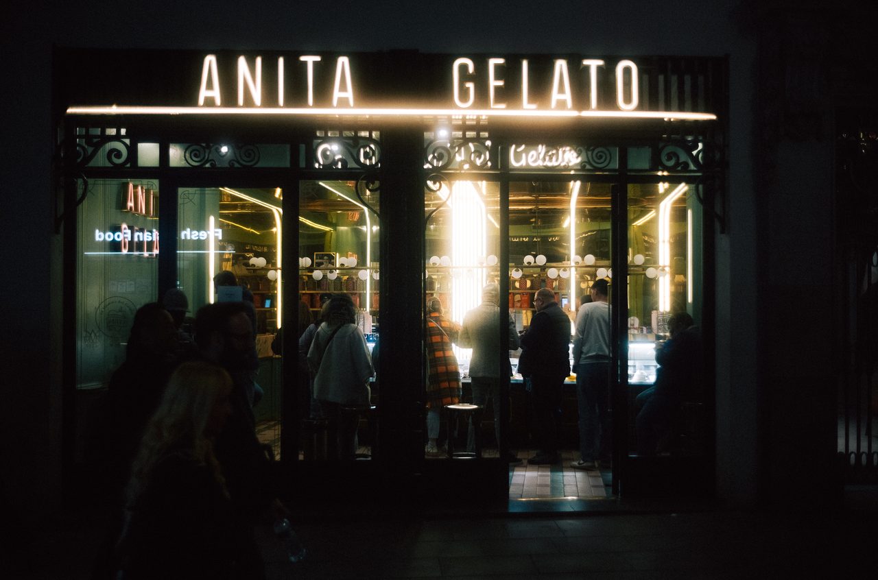 Gäste stehen nachts vor dem hell erleuchteten Eingang einer Gelateria.