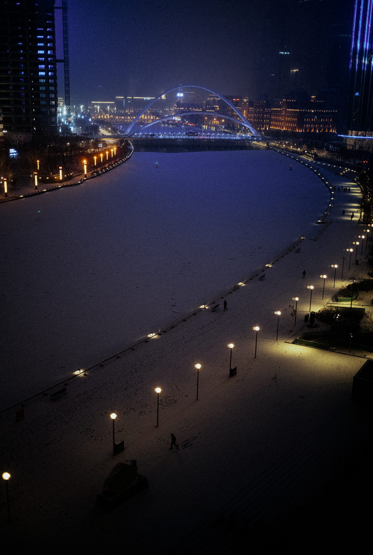 Nächtlicher Blick auf eine geschwungene Uferpromenade und beleuchtete Hochhäuser.