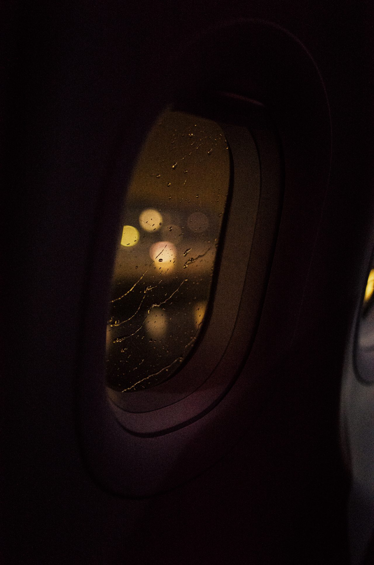 Regentropfen auf einem Flugzeugfenster vor unscharfen Lichtern bei Nacht.