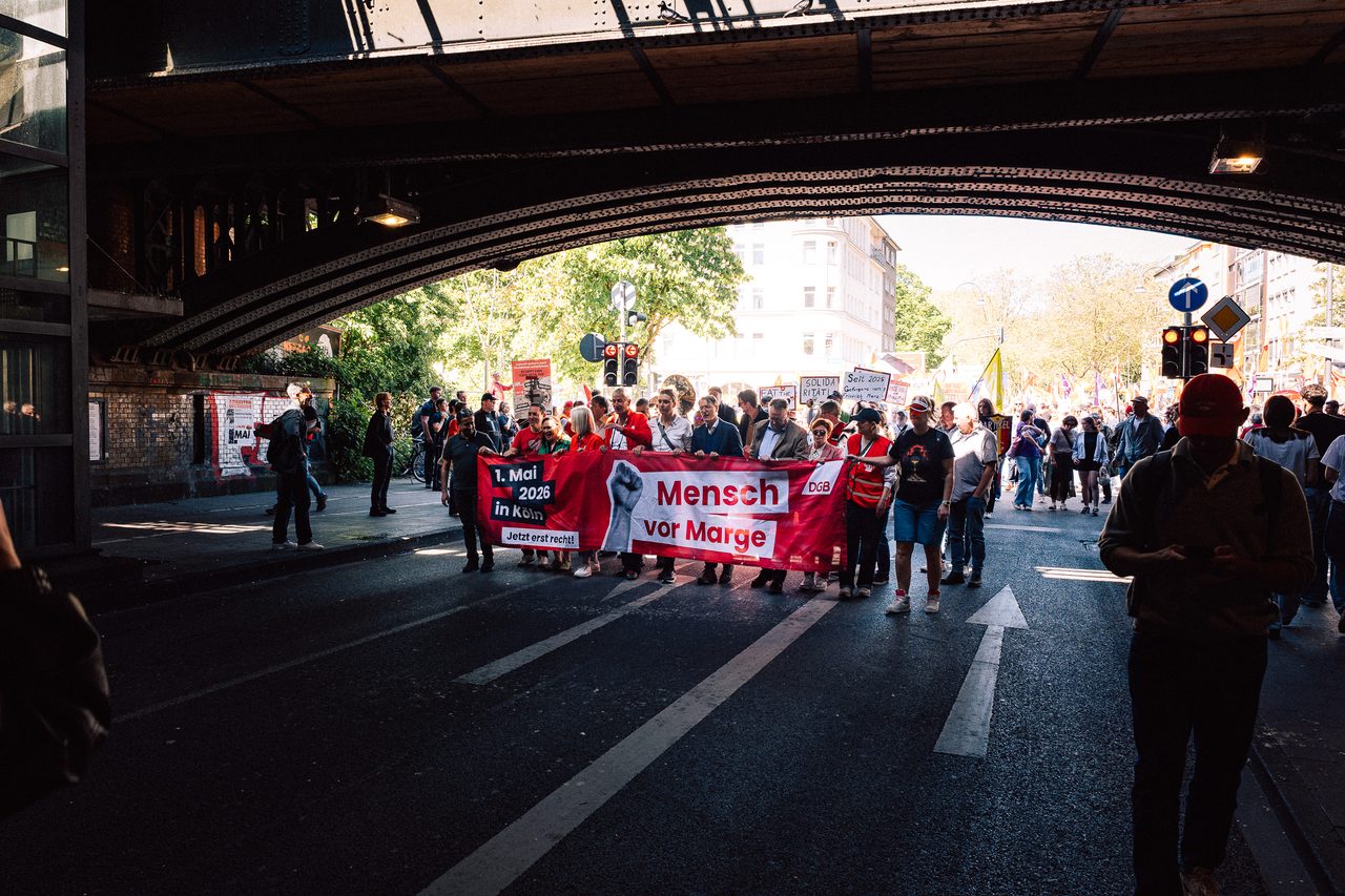 Demonstrationszug zieht mit dem Banner ‚Mensch vor Marge‘ unter einer Brücke hindurch