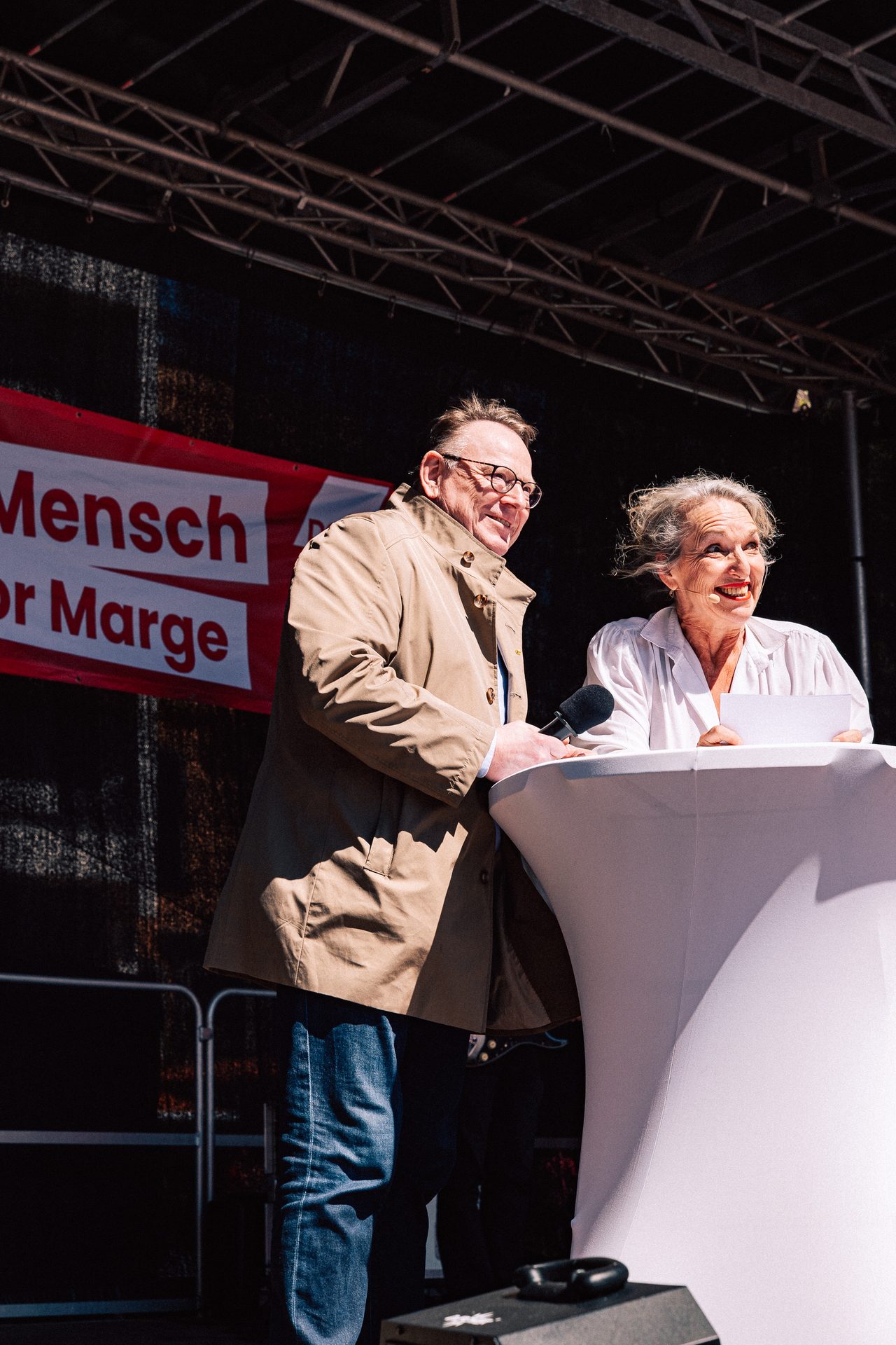 Mann und Frau lachen gemeinsam am Rednerpult auf einer Bühne