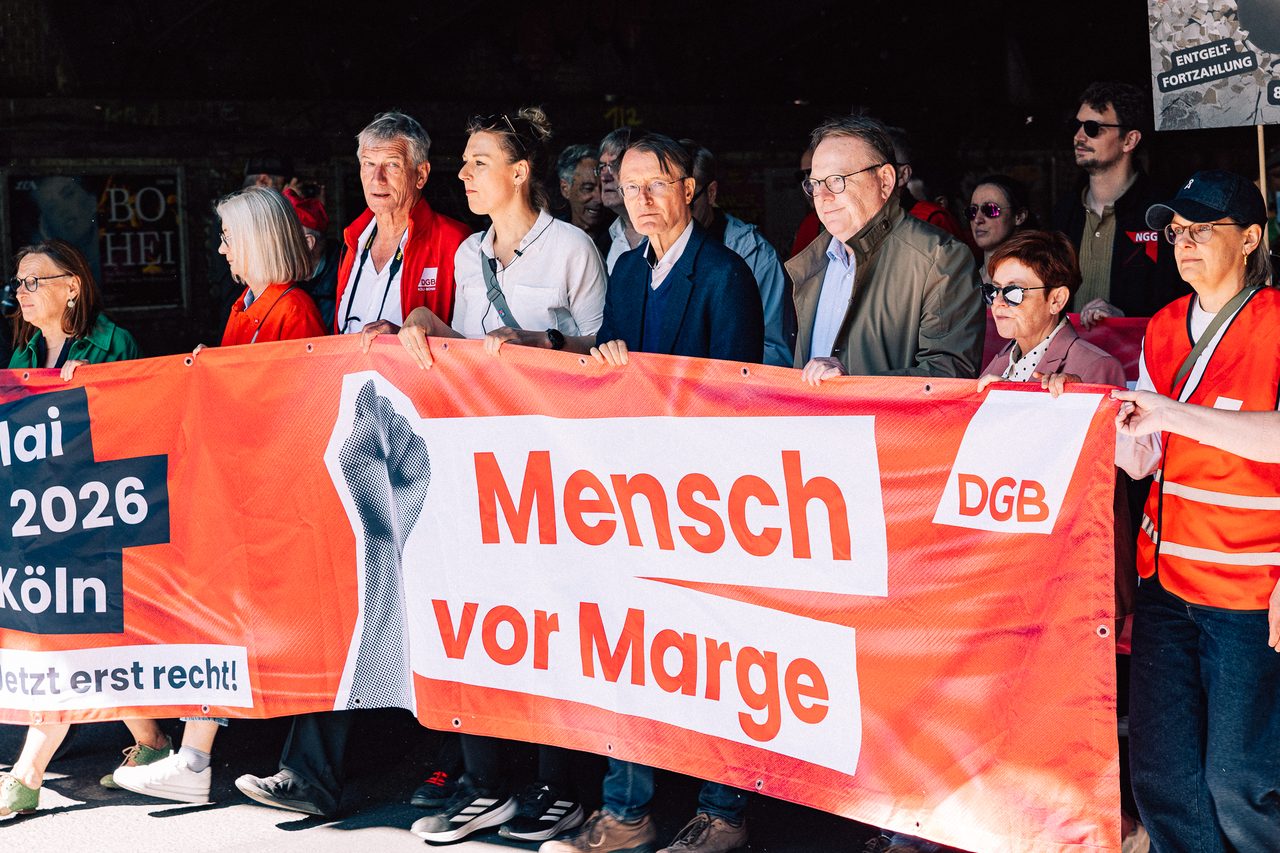 Teilnehmende halten gemeinsam das rote DGB-Banner ‚Mensch vor Marge‘