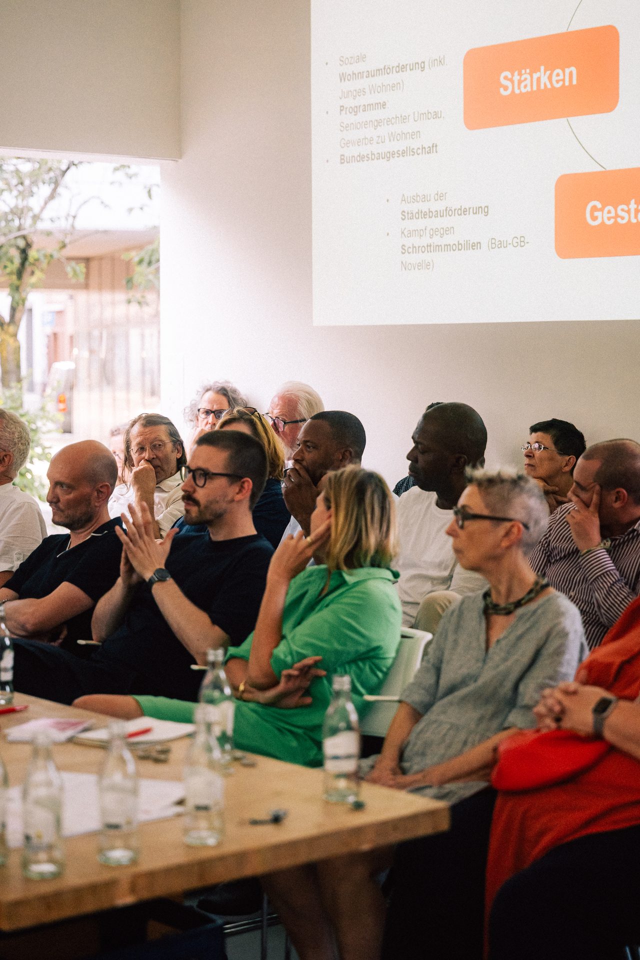Teilnehmende hören unter einer Projektion zur Wohnungspolitik aufmerksam zu