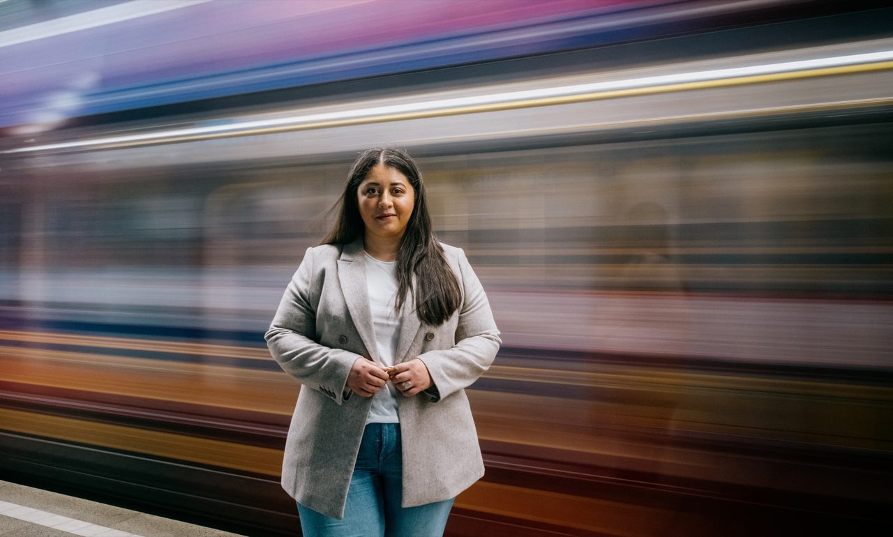 Sanae Abdi steht vor einer vorbeifahrenden Stadtbahn